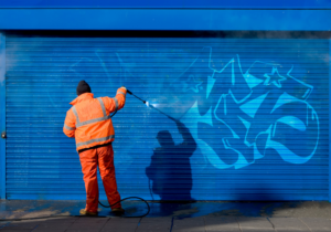 Graffiti removal services, worker removing graffiti from blue building